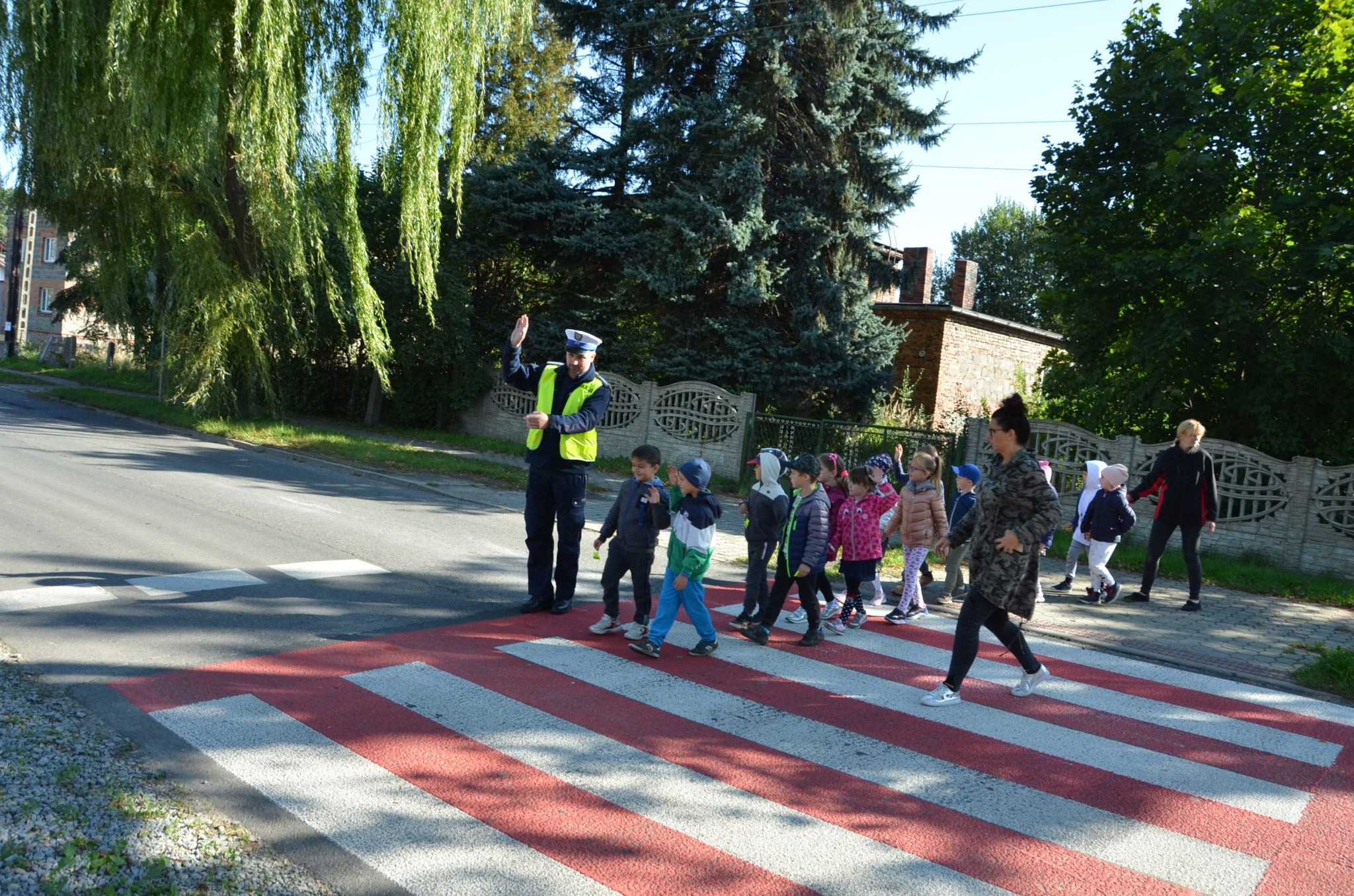 grupa przedszkolaków przechodzi przez jezdnie w asyście policjanta i opiekunki