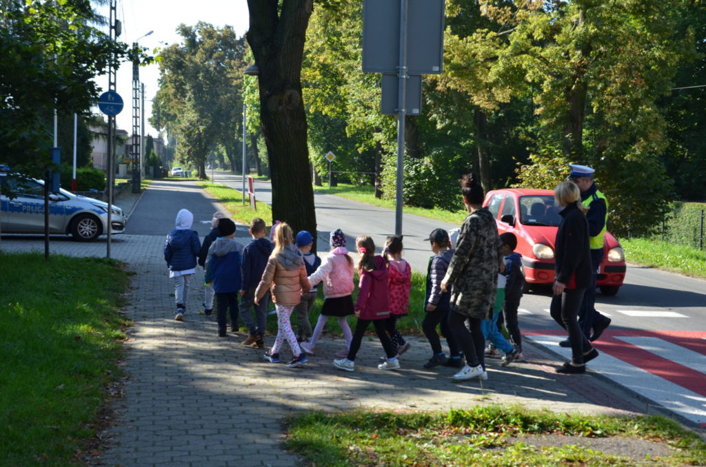 grupa przedszkolaków przechodzi przez jezdnie w asyście policjanta i opiekunki