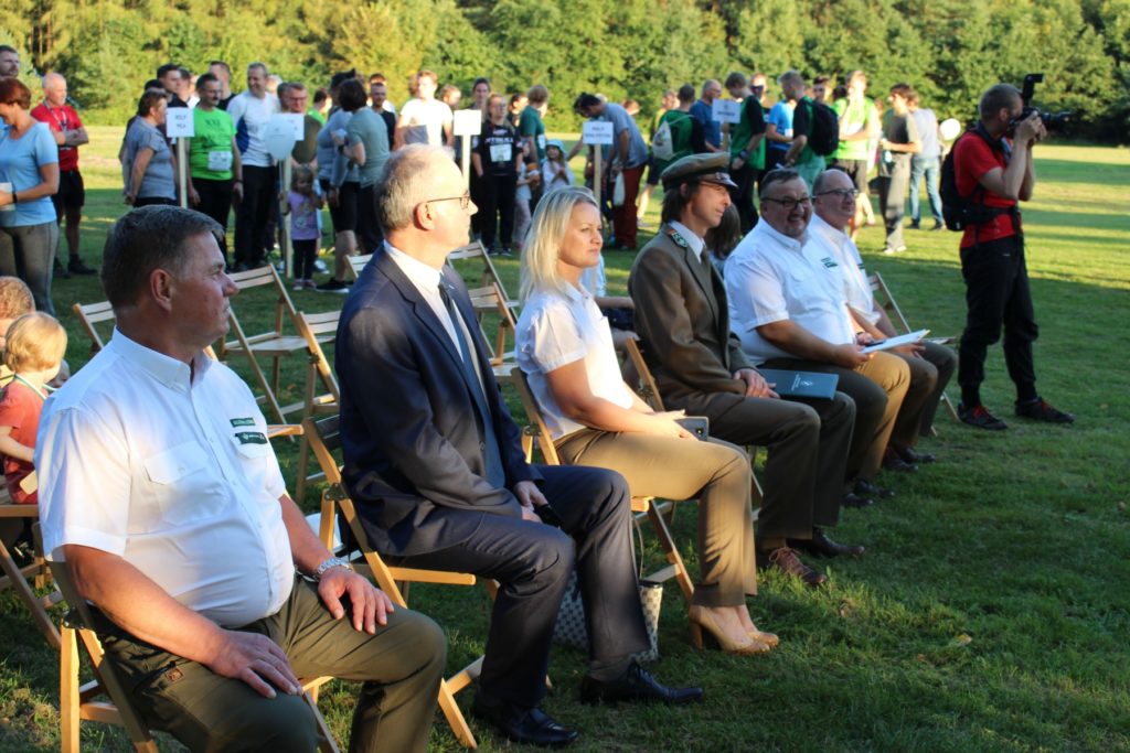 klika osób siedzących na krzesłach, za nimi kilkadziesiąt osób 