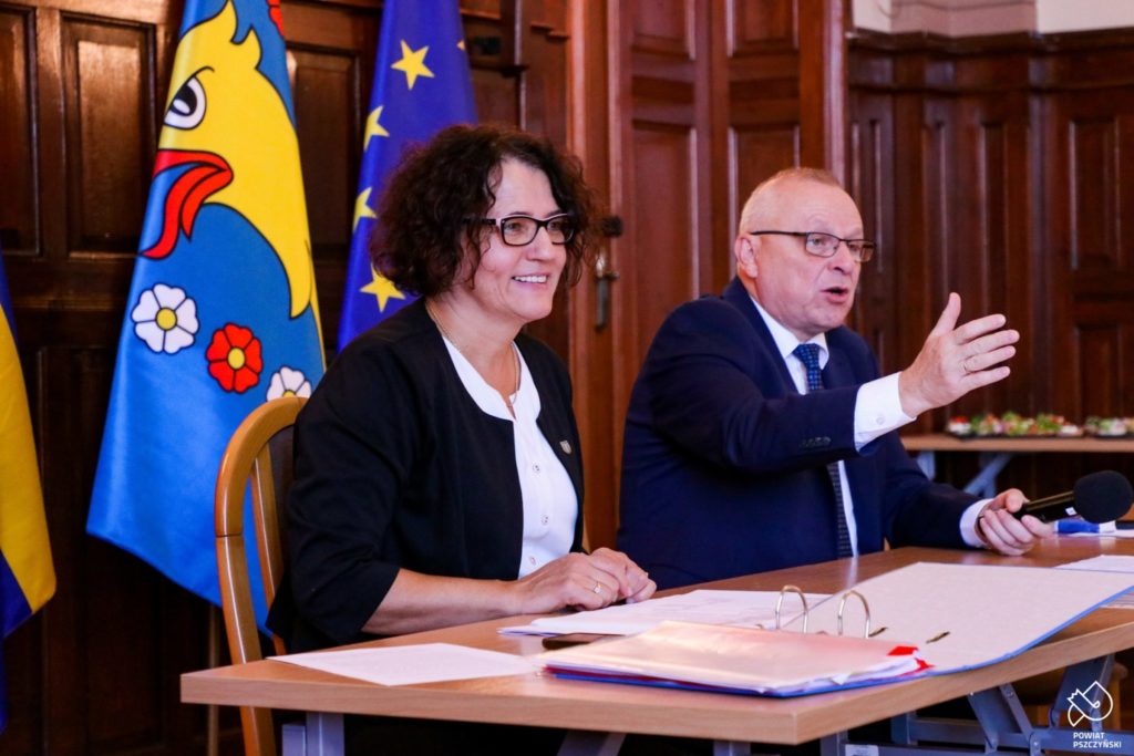 kobieta i mezczyzna siedzą stole, za nimi flagi UE i starostwa