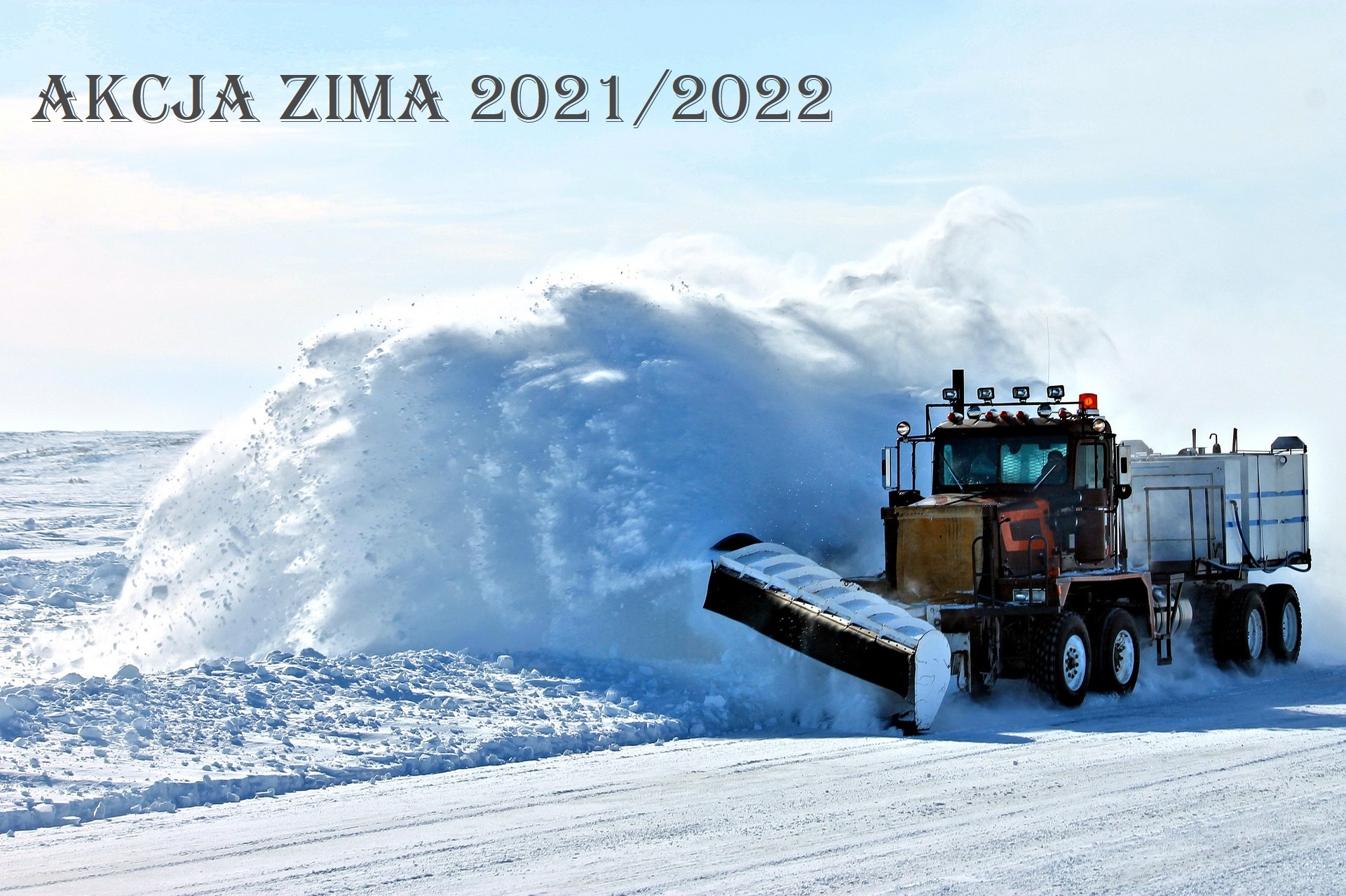 samochód ciężarowy z pługiem odśnieża drogę zasypaną śniegiem, słoneczny dzień, na górze napis Akcja Zima 2021/2022