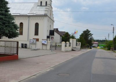 asfaltowa ulica wzdłóż ktrórej położony jest chodnik i kościół po lewej stronie
