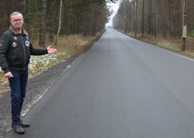 mężczyzna stojący przy skraju drogi asfaltowej pokazujący gestem ręki drogę