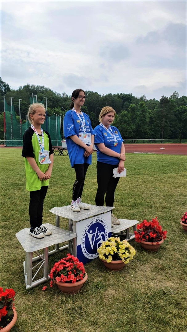 Trzy dziewczyny stojące na podium, wszystkie mają medale na szyi