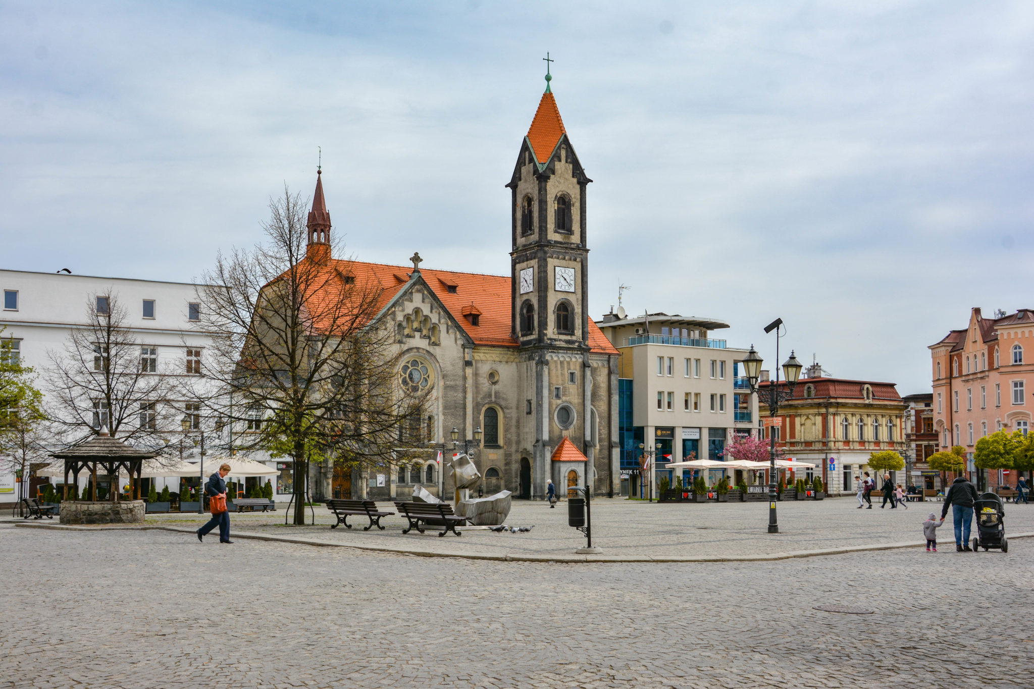 na pierwszym planie nawierzchnia z kostki, w tle zabudowa z dominującą wieżą kościoła