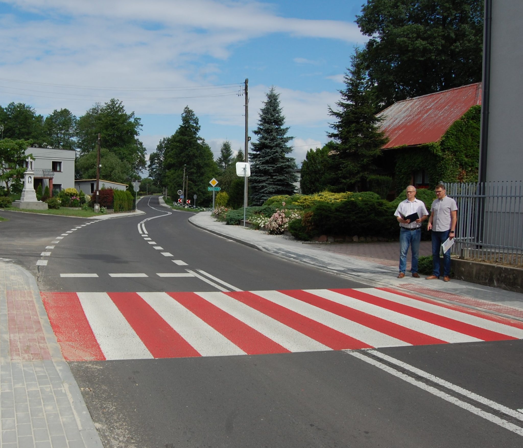 droga asfaltowa z oznakowanym przejściem dla pieszych przy którym stoją dwaj mężczyźni