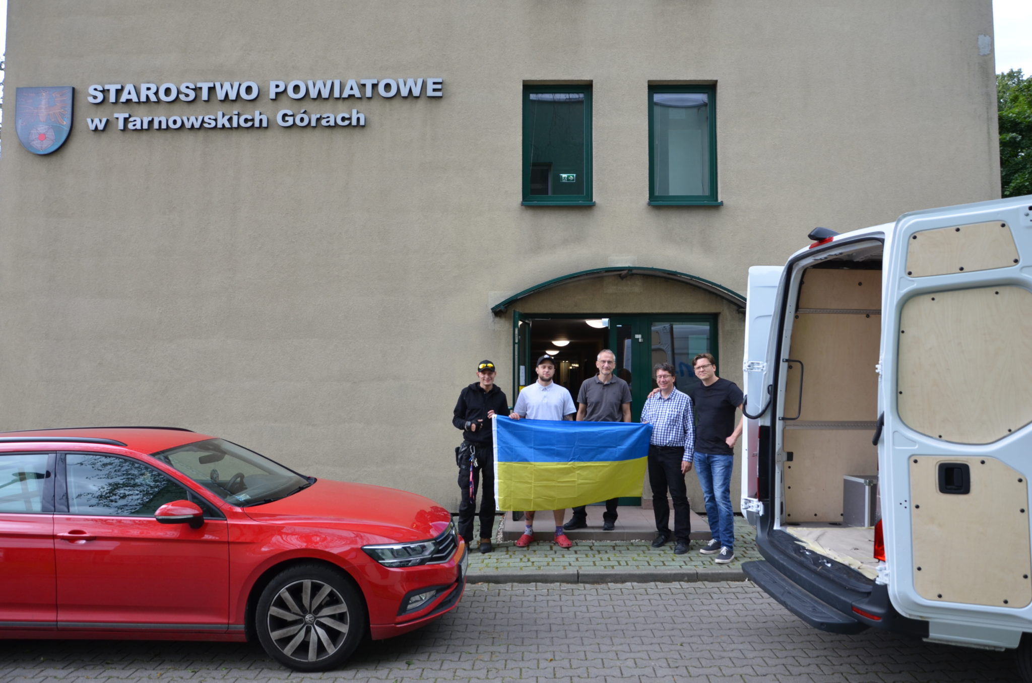 kilku mężczyzn stoi przed budynkiem starostwa z flagą Ukrainy