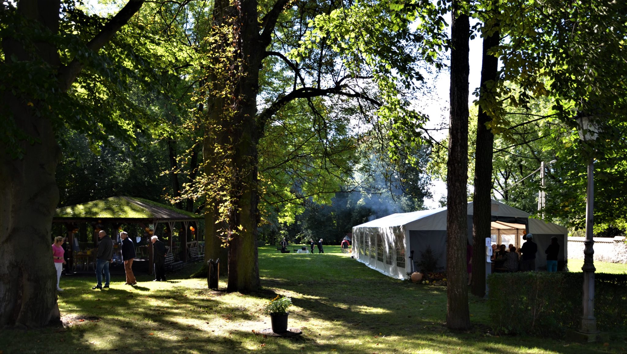 Teren zieleni z altanką po lewej stronie. Po prawej stronie duży, jasny, ogrodowy namiot.