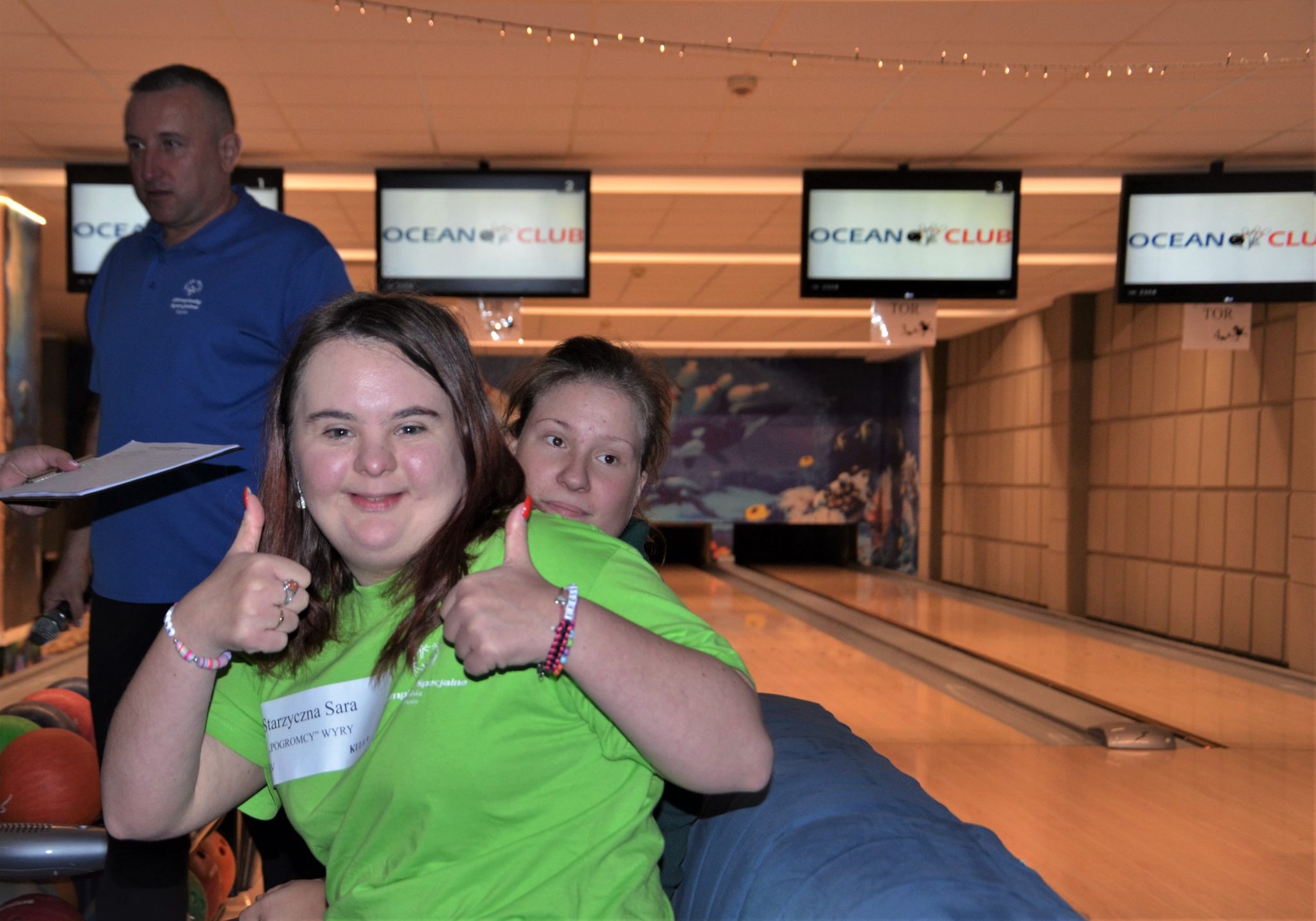 Dziewczyna w zielonej koszulce na pierwszym planie, za nią tor bowlingowy.