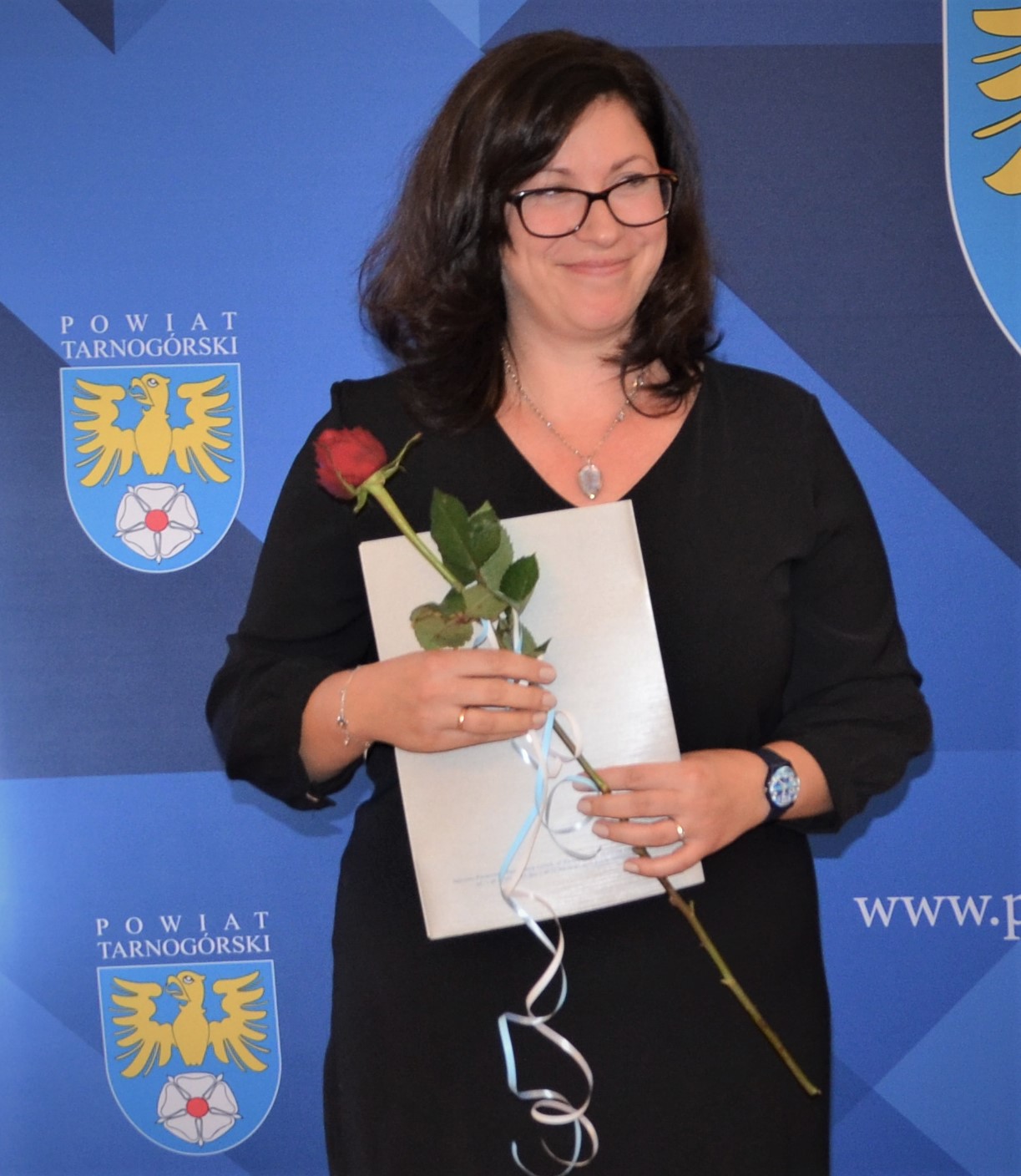 Nauczycielka z dokumentem w dłoni oraz z czerwoną różą.