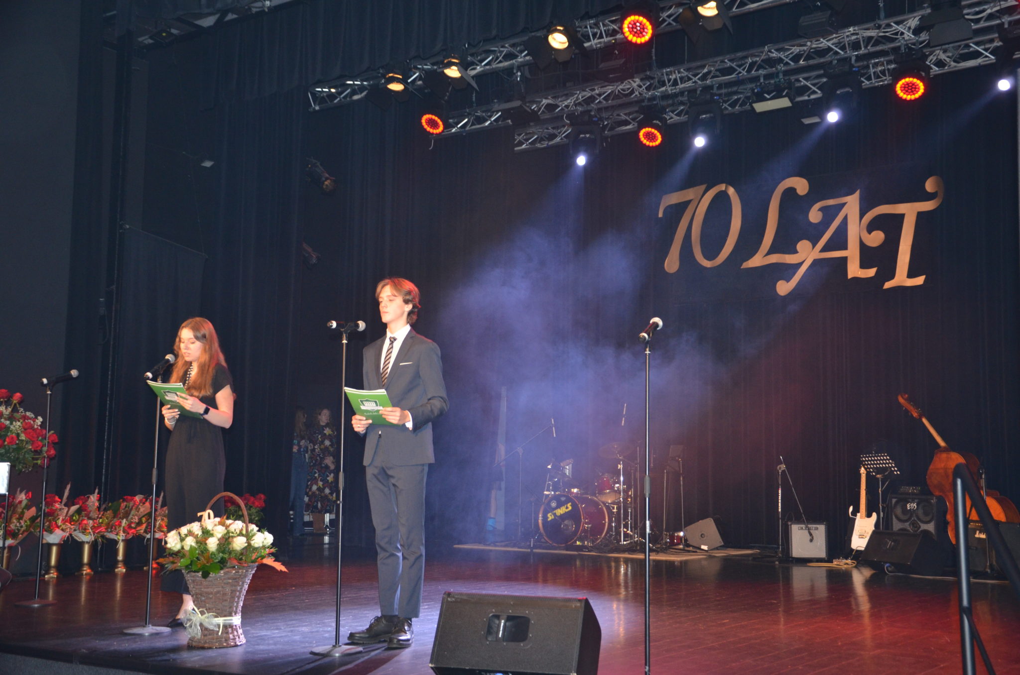 Dwie osoby stoją na scenie, w tle duży napis 70 lat.