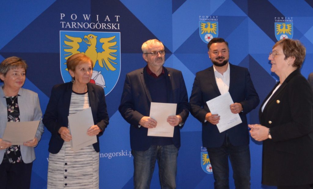Grupa osób z dokumentami, w tle baner z napisem powiat tarnogórski.