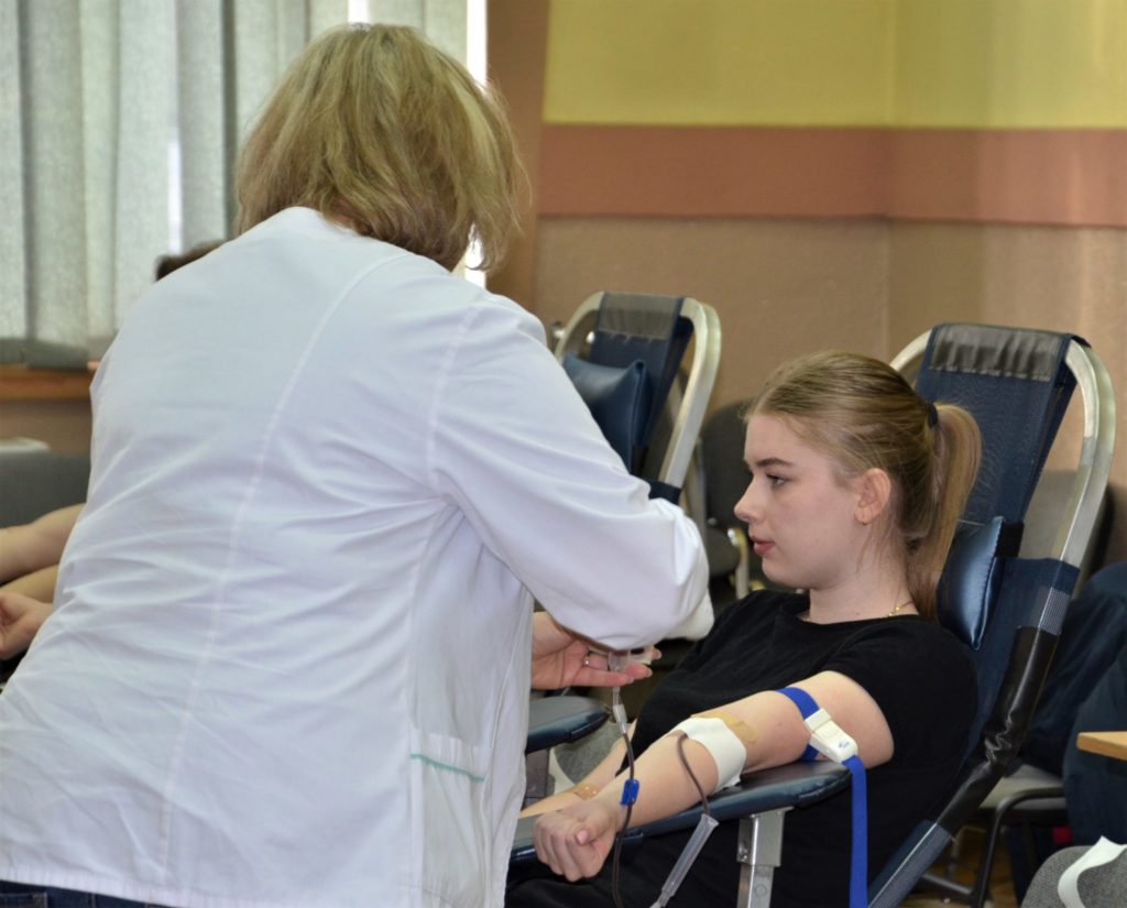 Dziewczyna podczas pobierania krwi, przy której stoi kobieta w fartuchu medycznym.