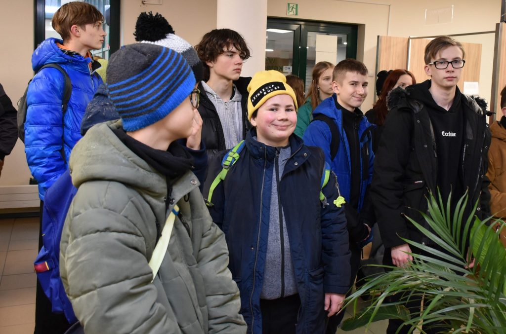 Grupa młodzieży w pomieszczeniu, w centralnej części stoi uśmiechnięty chłopiec w czapce.