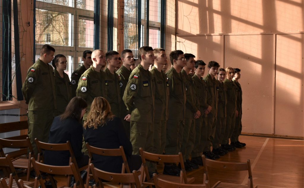 Grupa młodzieży w mundurach, wszyscy stoją obok siebie w kilku rzędach.