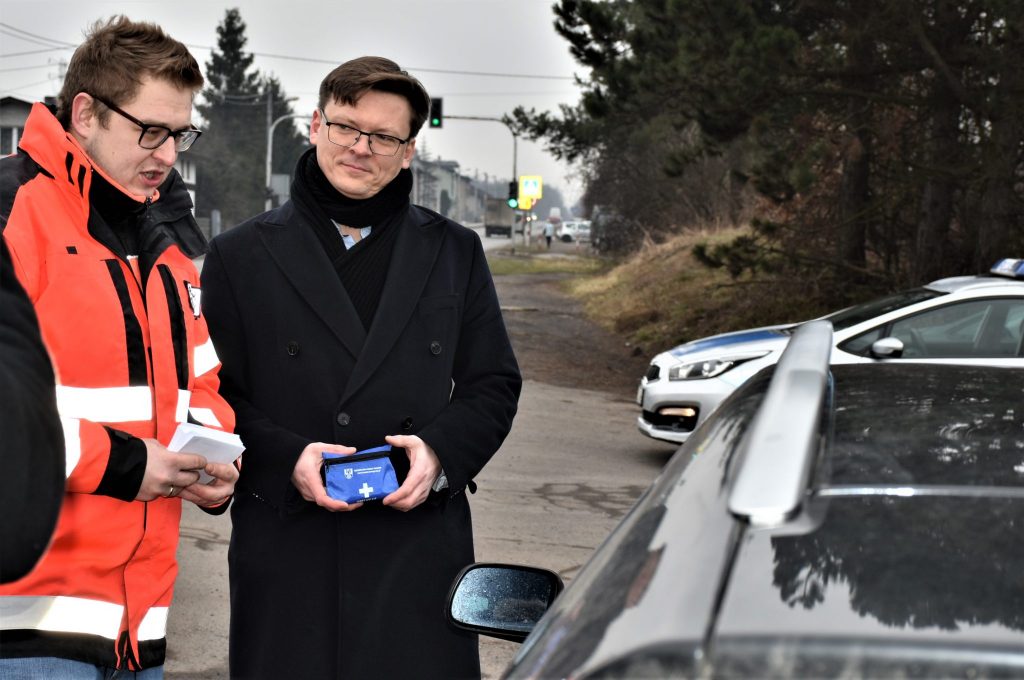 Stanisław Torbus i ratownik medyczny stoją przy samochodzie znajdującym się na poboczu.