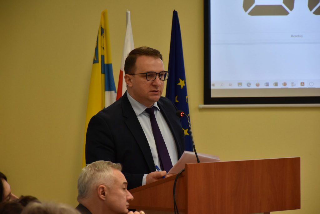 Przewodniczący Rady Powiatu przy mównicy, w tle trzy flagi.