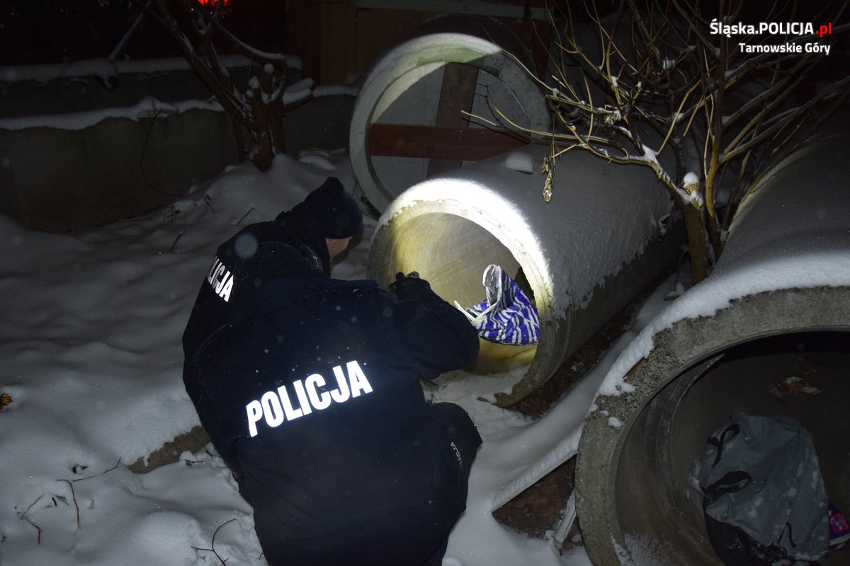 Dwoje funkcjonariuszy policji podczas pracy w terenie. Jedna z osób świeci latarką do betonowego kręgu, w którym znajduje się foliowa torba.