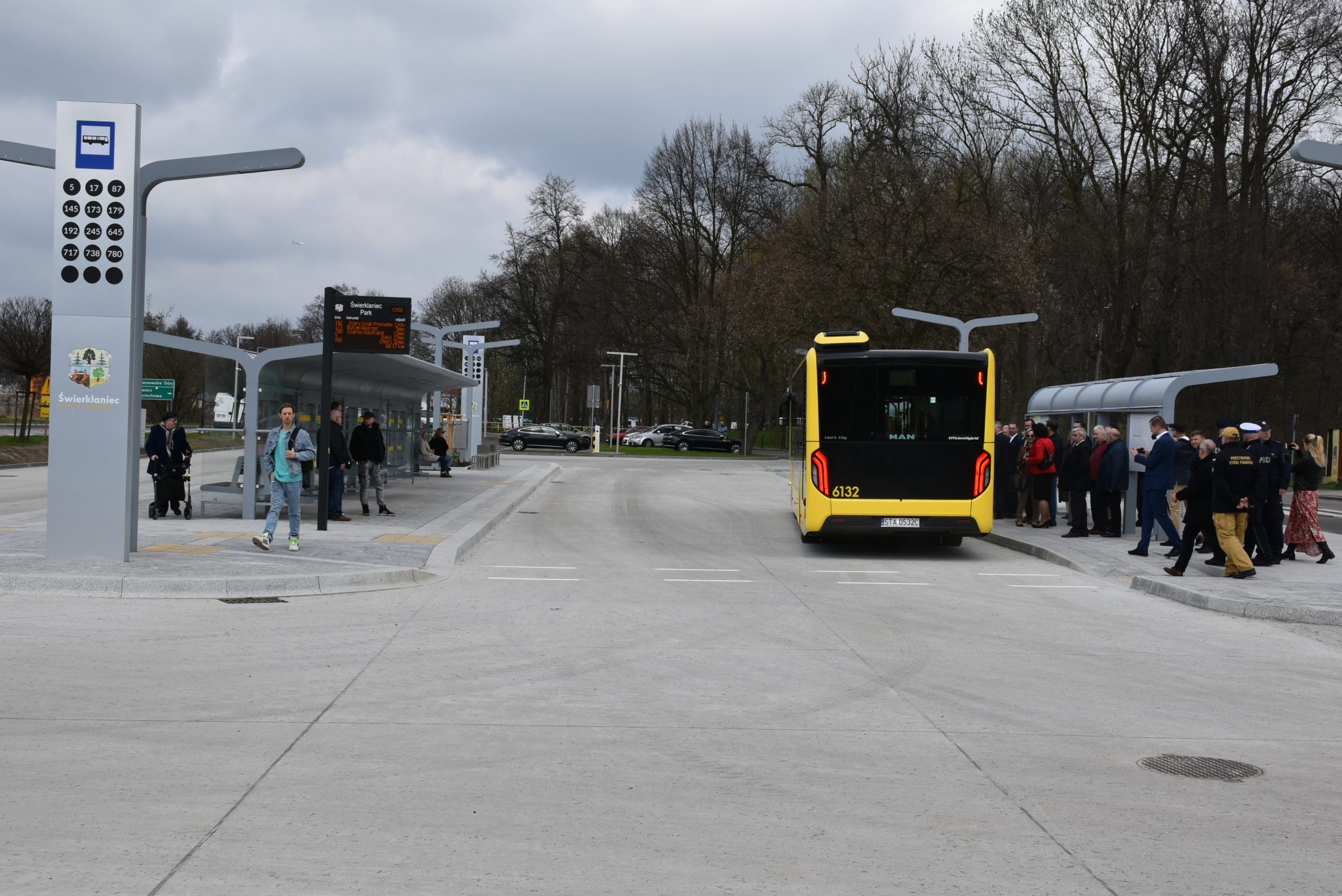 Przystanki autobusowe. Na jeden z przystanków podjeżdża autobus, do którego zmierza duża grupa osób.