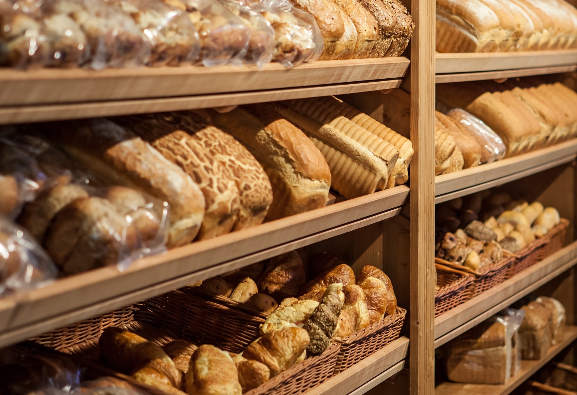 Bochenki chleba i inne pieczywo, które leży na drewnianych półkach.