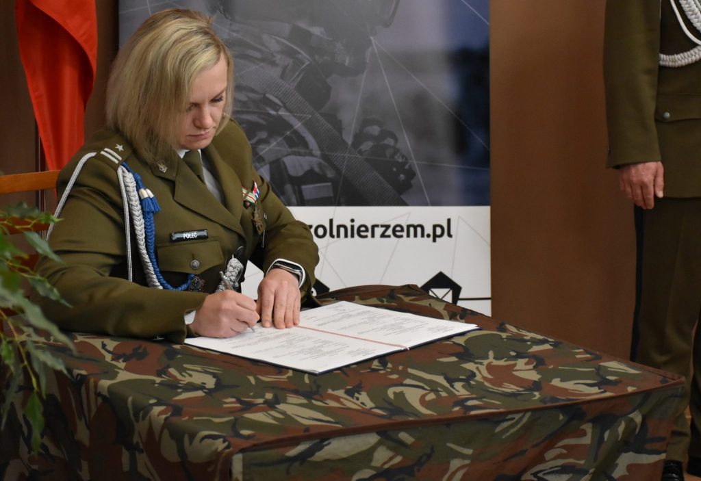 Kobieta w mundurze siedzi przy stoliku i podpisuje dokument.