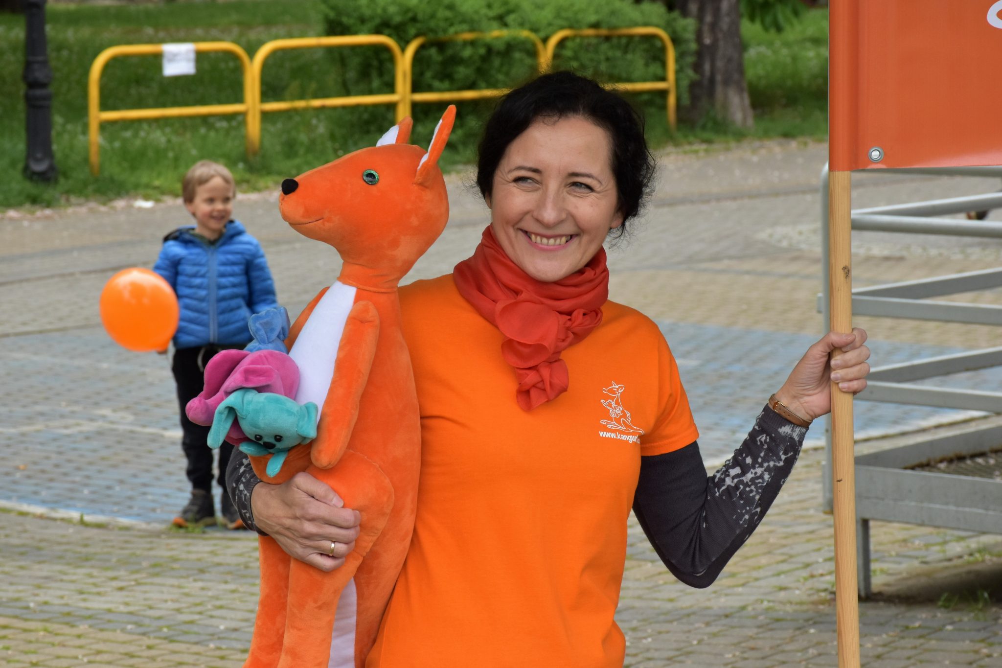 kobieta w pomarańczowej koszulce trzyma w reku maskotkę kangura