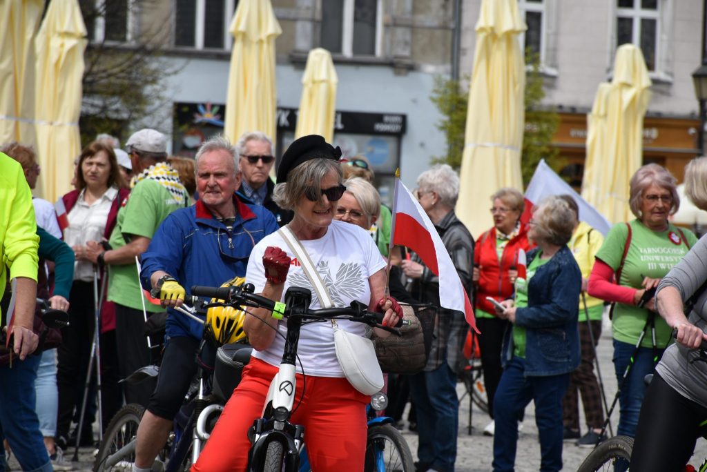 Grupa osób z rowerami. Część z osób trzyma biało-czerwone flagi.l