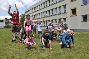 Grupa dzieci znajdująca się na trawniku. W tle duży budynek szkoły.