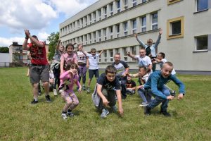 Grupa dzieci znajdująca się na trawniku. W tle duży budynek szkoły.