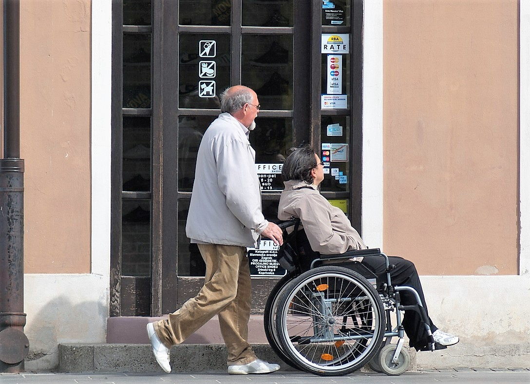 mężczyzna prowadzi wózek z niepełnosprawną kobietą