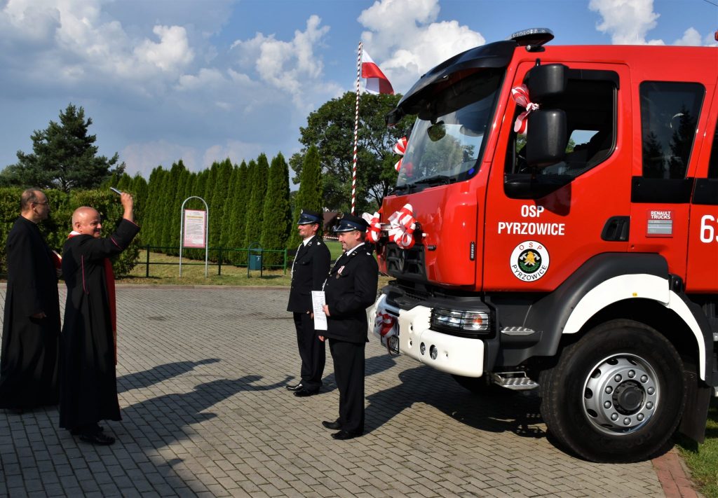 Samochód ze znakiem osp pyrzowice, przed którym stoją dwaj mężczyźni w mundurach.