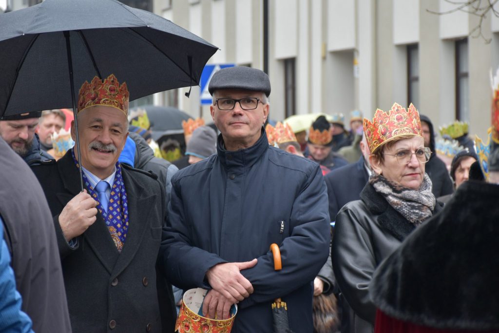 Na pierwszym planie mężczyzna w okularach. Po prawej stronie Starosta Tarnogórski. W tle wysoka zabudowa oraz duża grupa osób.