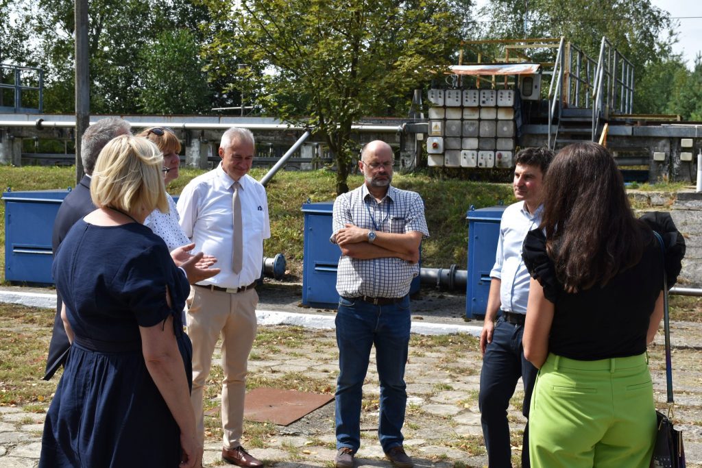 Grupa osób podczas rozmowy zgromadzona w okręgu. W tle urządzenia techniczne.