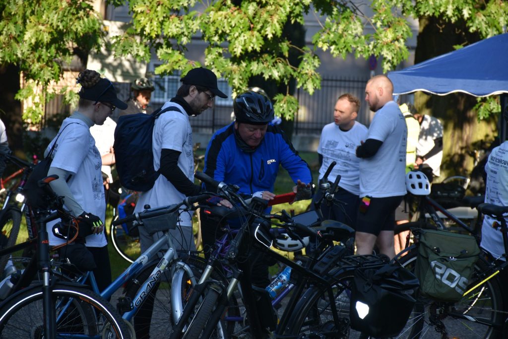 Grupa osób w strojach sportowych stojąca przy rowerach.