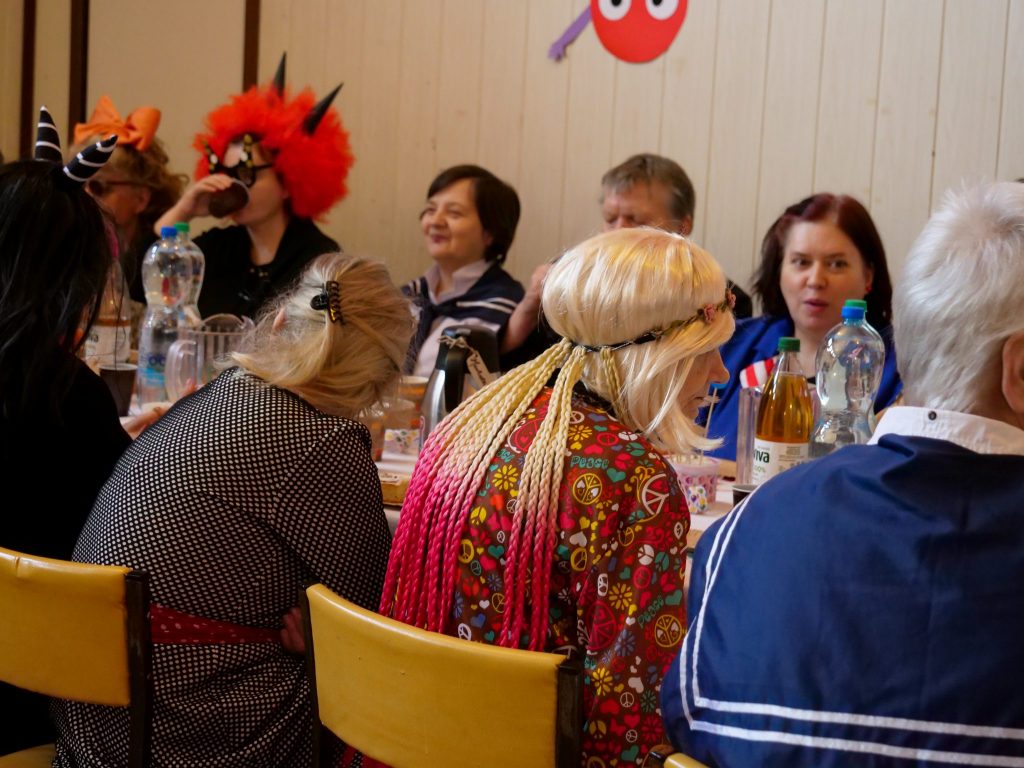 dorośli ludzie przebrani w kolorowe stroje, siedzą przy stole, 