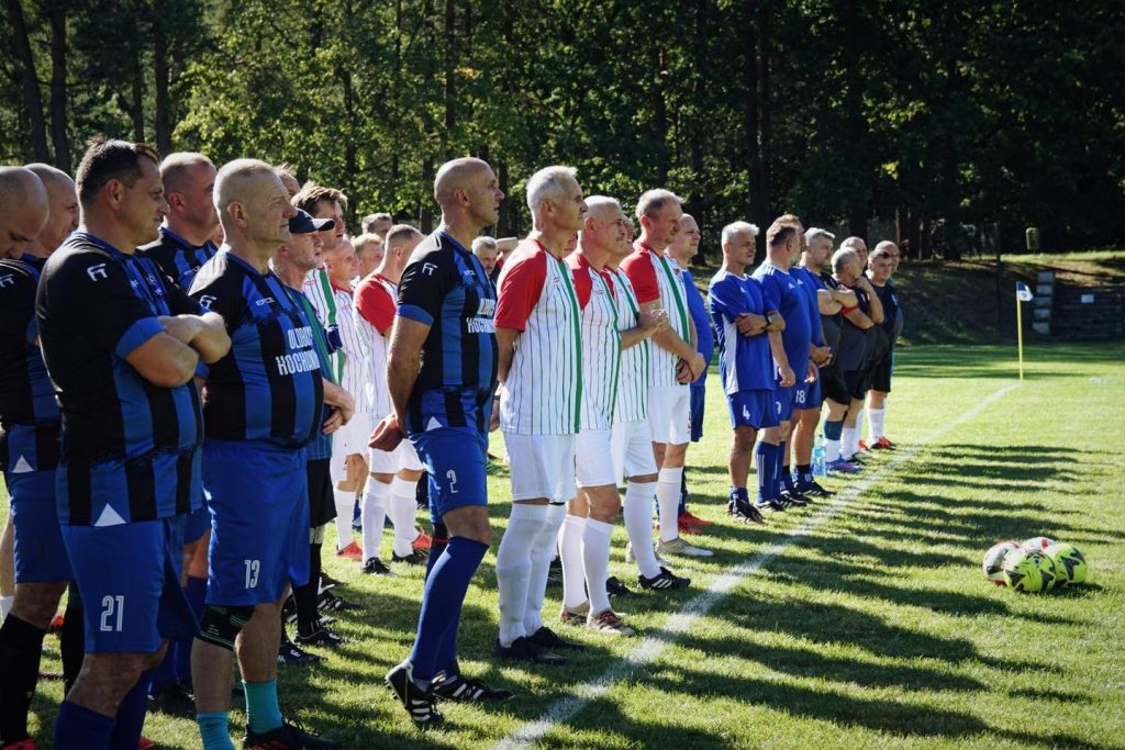 grupa piłkarzy stoi w rzędzie, na murawie, przed nimi piłki
