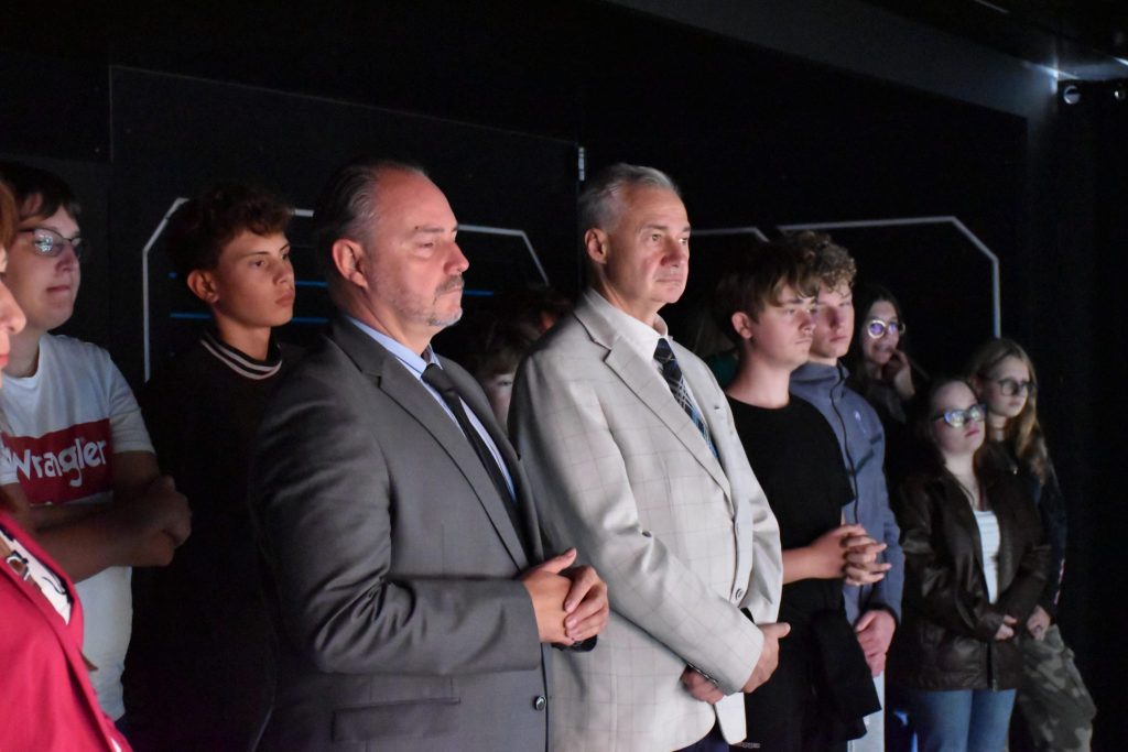 w pomieszczeniu multimedialnym dwóch mężczyzn w garniturach oraz uczniowie ze szkoły, zwróceni w prawą stronę