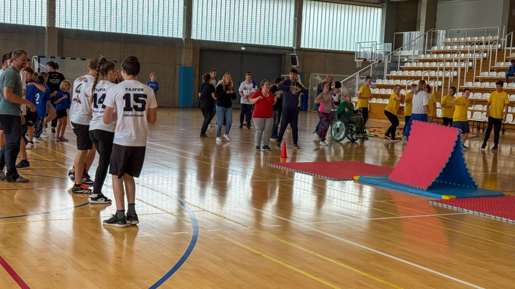 drużyny sportowe, rywalizują w konkurencji sportowej, na boisku materace piankowe, w tle fragment trybun 