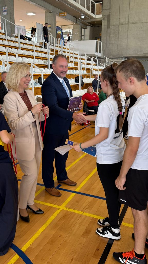 kobieta i mężczyzna wręczają medale zawodnikom sportowym, w tle trybuny