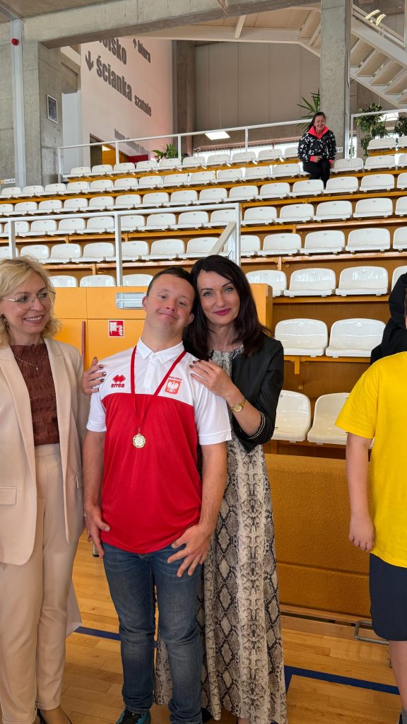 dwie kobiety i chłopiec z niepełnosprawnością, w pomieszczeniu hali sportowej, w tle trybuny