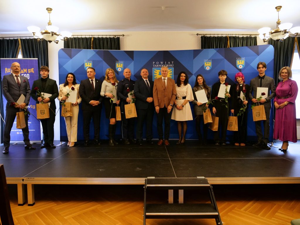 na scenie grupa osób, większość z nich trzyma w ręku torby prezentowe