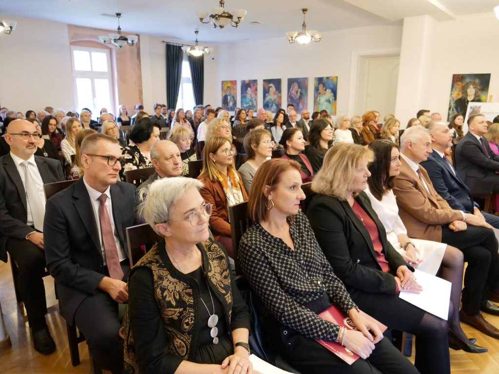 duża grupa osób siedzi na widowni, osoby z przodu w ręce trzymają dokumenty