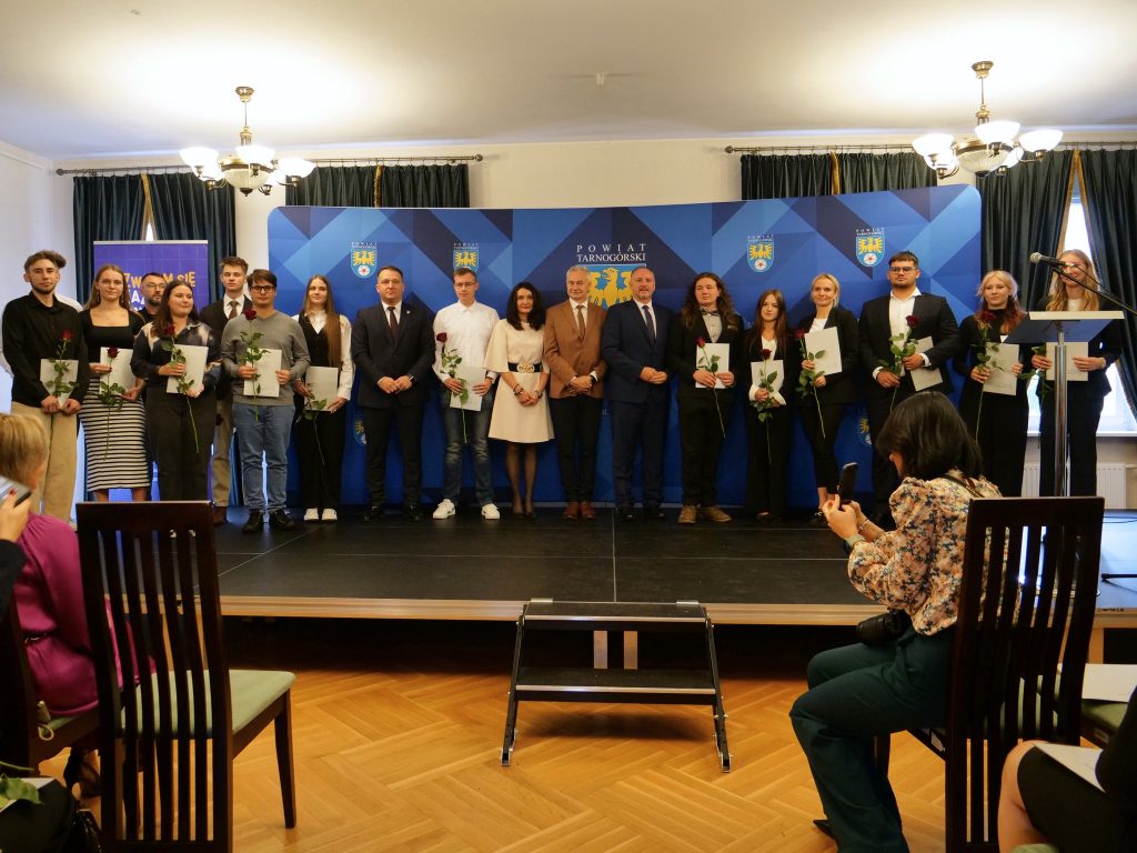grupa osób na scenie, większość z nich trzyma w rękach dyplomy, z przodu fragment osób na widowni