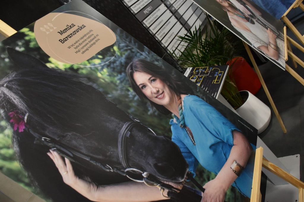 zdjęcie obrazu kobiety z koniem, na sztaludze, w tle tablica informacyjna i kwiatek