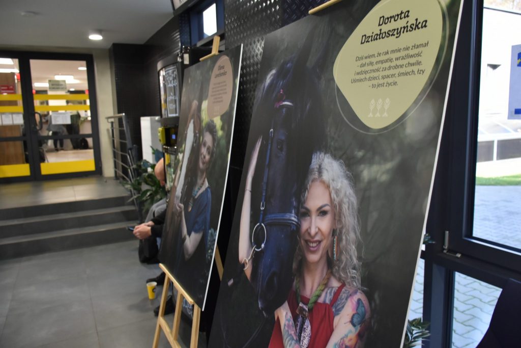 w holu, obrazy kobiet przytulają konie, obrazy są na sztaludze, w tle drzwi przesuwne