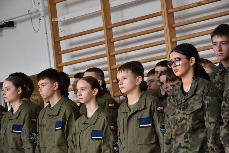 grupa uczniów stoi w szeregach w mundurach wojskowych, za nimi w tle drabinki
