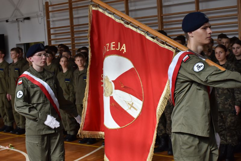 uczniowie w mundurach , jeden z nich niesie sztandar