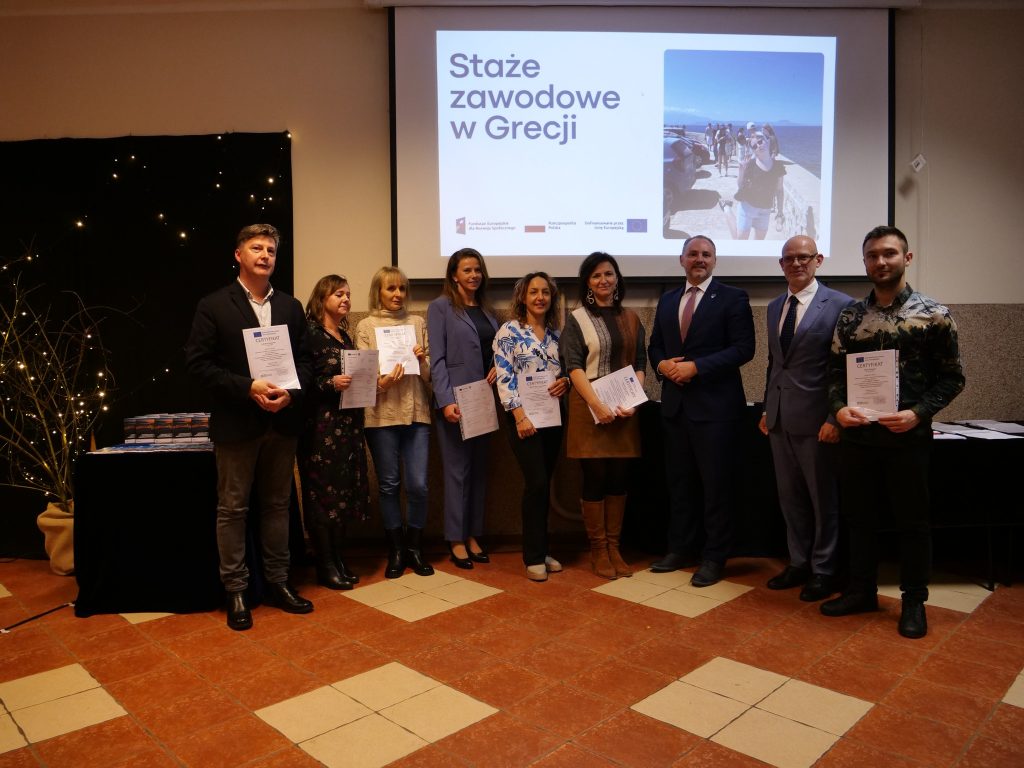 grupa nauczycieli i dwóch mężczyzn w garniturze pozują do zdjęcia, nauczyciele w rękach trzymają dyplomy