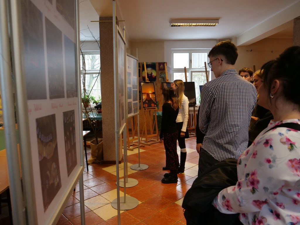 grupa osób, w pomieszczeniu ogląda wystawę obrazów