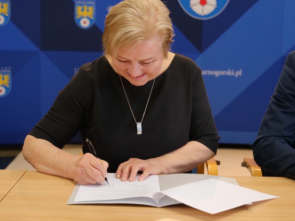 kobieta siedzi przy stole, na stole dokumenty, podpsiuje dokumenty